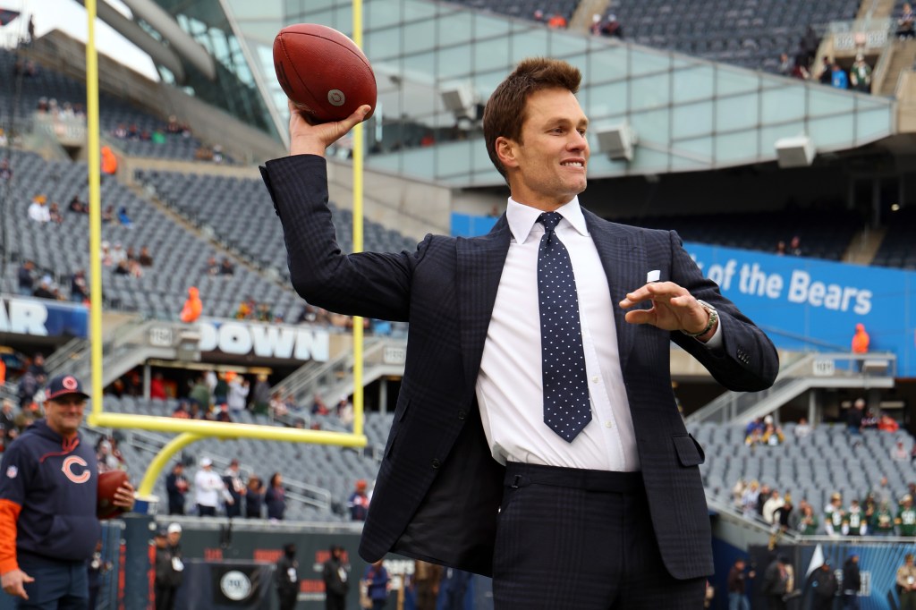 Tom Brady in a suit gets ready to throw a football.