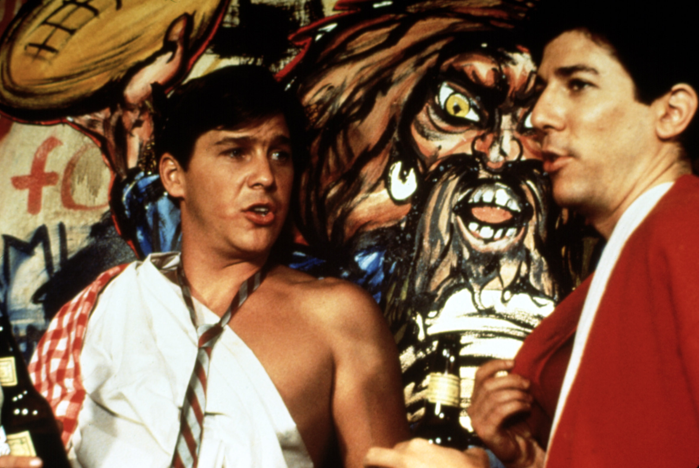 Tim Matheson wearing a toga and necktie, standing next to Peter Riegert in a scene from "Animal House"