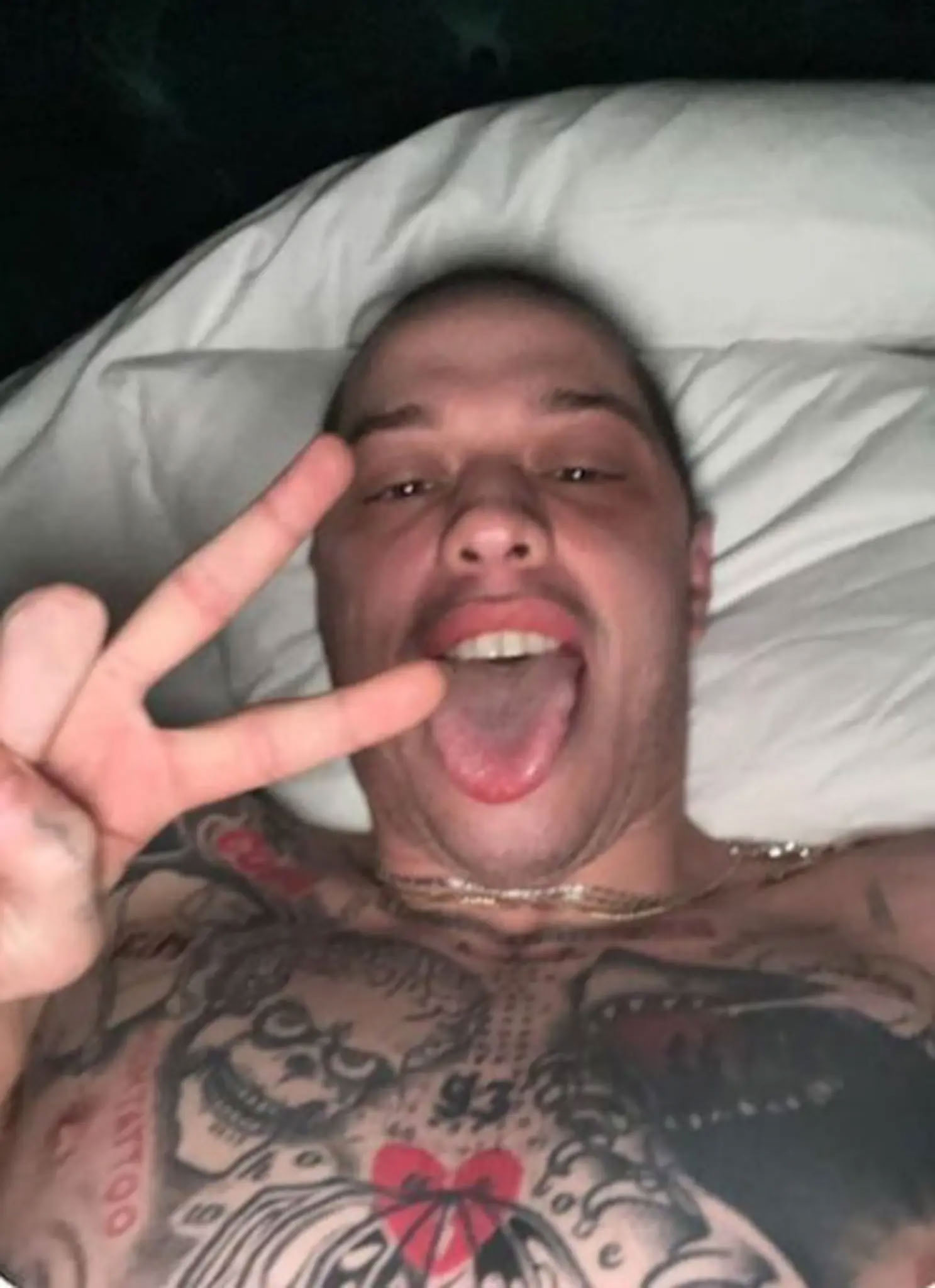 Pete Davidson flashing a peace sign from bed