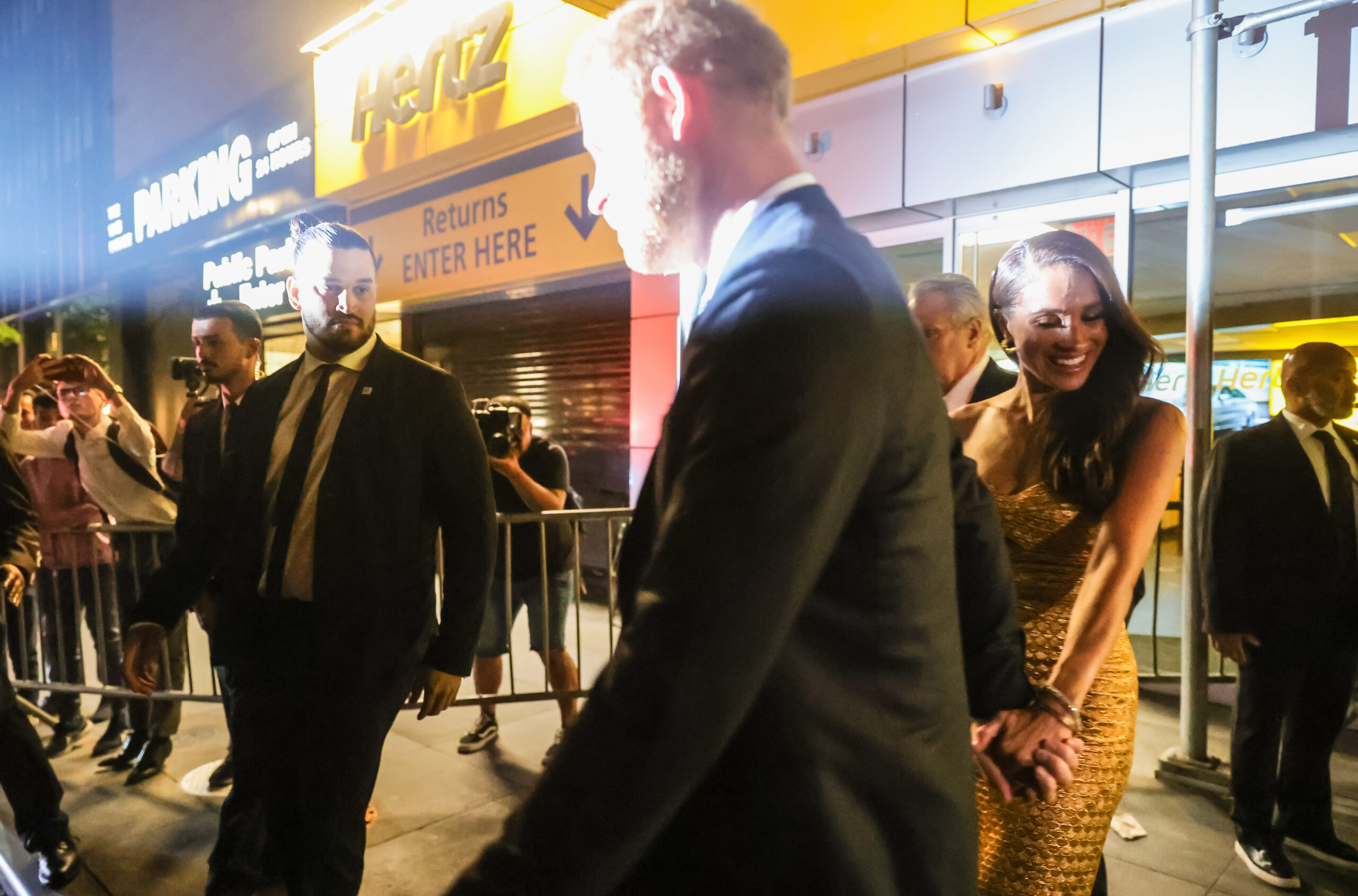 Meghan Markle and Prince Harry walking in New York to their car as cameras flash.