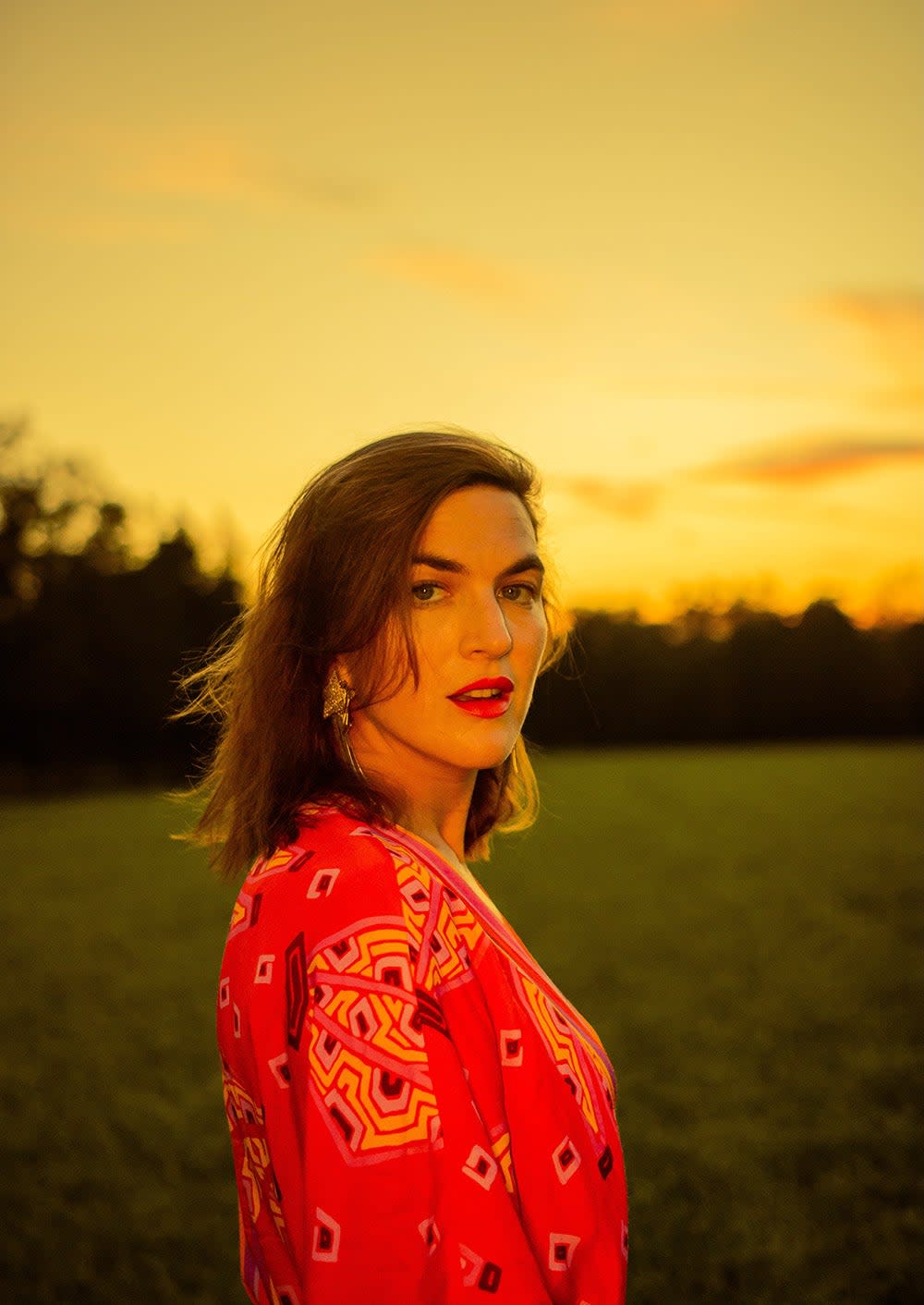 Laura Warshauer wearing a floral coral dress in a field during sunset.