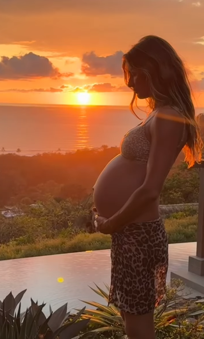 Gisele Bündchen holding her baby bump in front of a sunset.