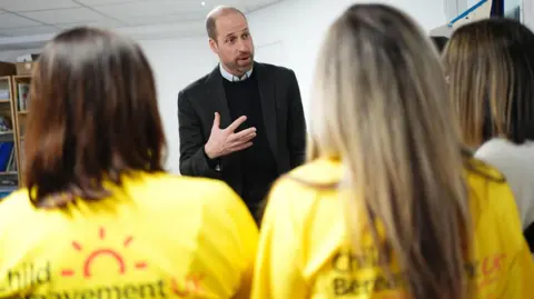 PA Media Prince William talks to a group of people. Two women  in yellow charity shirts have their back to the camera.