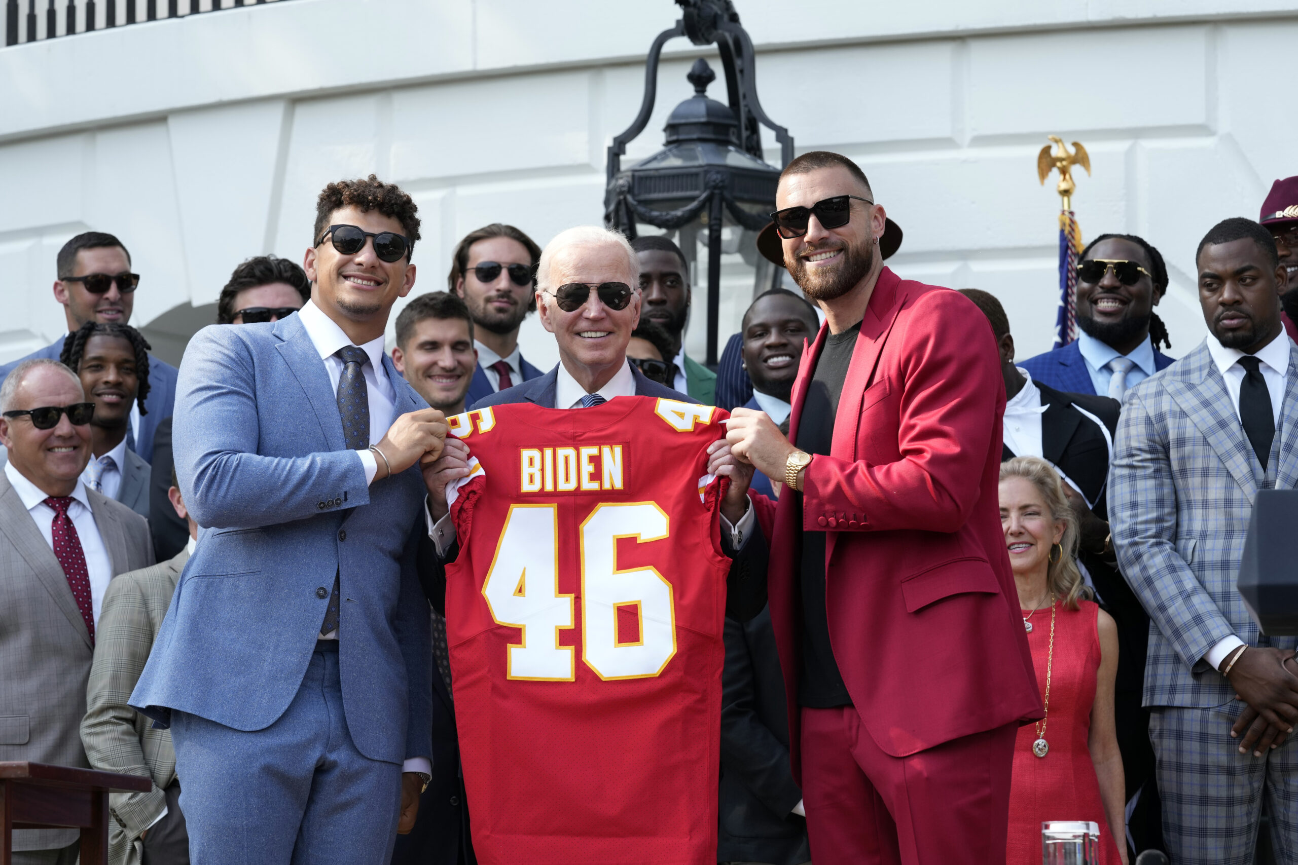 Patrick Mahomes and Travis Kelce holding up a football jersey with President Biden.